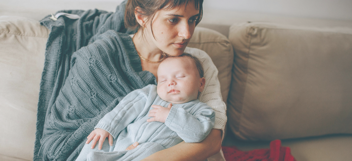 Ein ruhiges Baby liegt entspannt im Arm seiner Mutter, die es liebevoll hält. Das Bild symbolisiert die besondere Nähe und Fürsorge, die hochsensible Babys benötigen, um sich sicher und geborgen zu fühlen.