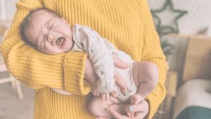 Eine Mutter hält ihr weinendes Baby im Arm. Das Baby liegt quer auf ihrem Unterarm und schreit, während die Mutter es sanft stützt und zu beruhigen versucht. Die Szene vermittelt Fürsorge und die Herausforderung, ein schreiendes Baby zu trösten.